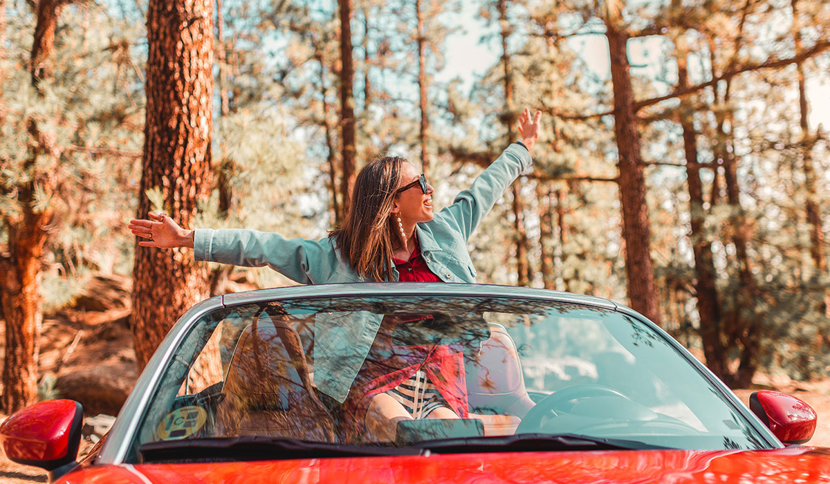 Woman sitting in the back of a convertible with her arms stretched wide